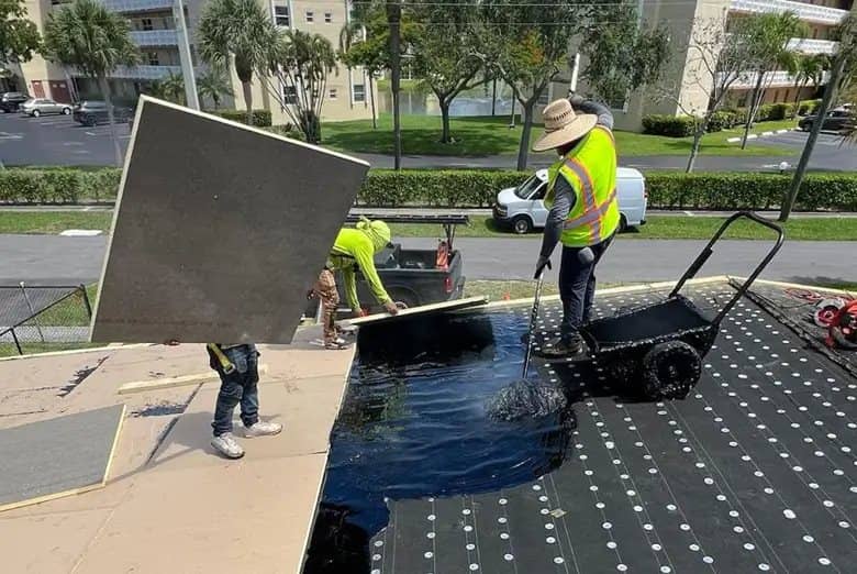 Roofing crew applying primer and installing underlayment on a flat roof