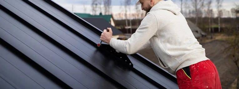 Roofer installing a dark metal roof panel