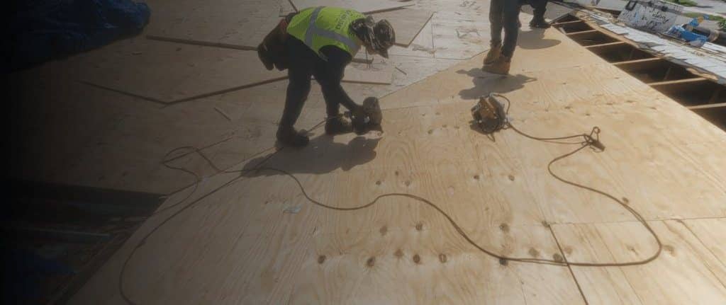 Crew installing new plywood decking during a roof replacement